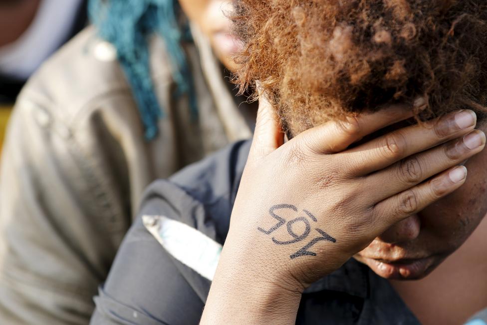 The identification number is seen written on a woman's hand as she rests with more than 1,000 migrants after they disembarked from the British assault ship HMS Bulwark at the Sicilian port of Catania