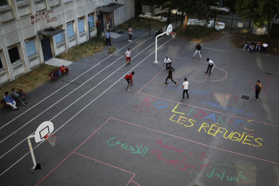 Migrants play soccer on the basketball court of the Guillaume-Bude secondary school, on which is painted in French "Solidarity with refugees" in Paris