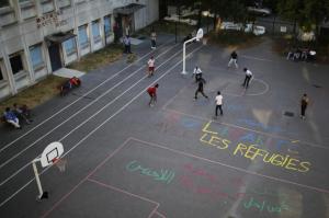 Migrants play soccer on the basketball court of the Guillaume-Bude secondary school, on which is painted in French "Solidarity with refugees" in Paris